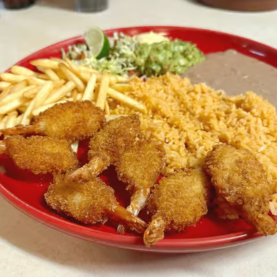 Breaded fried shrimp served with rice, beans, French fries, salad, and lime on a red plate.
