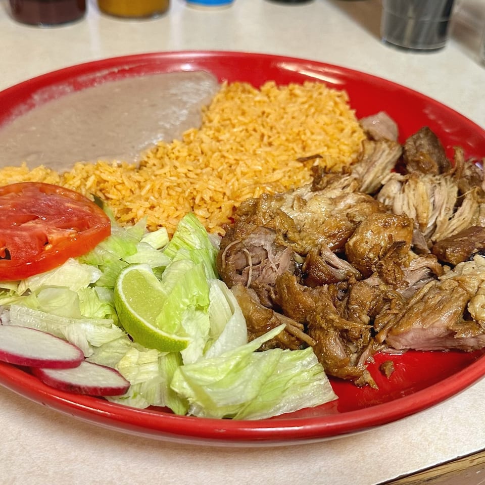 A red plate of Tacos El Rey carnitas with rice, refried beans, lettuce, tomato, radish, and lime.