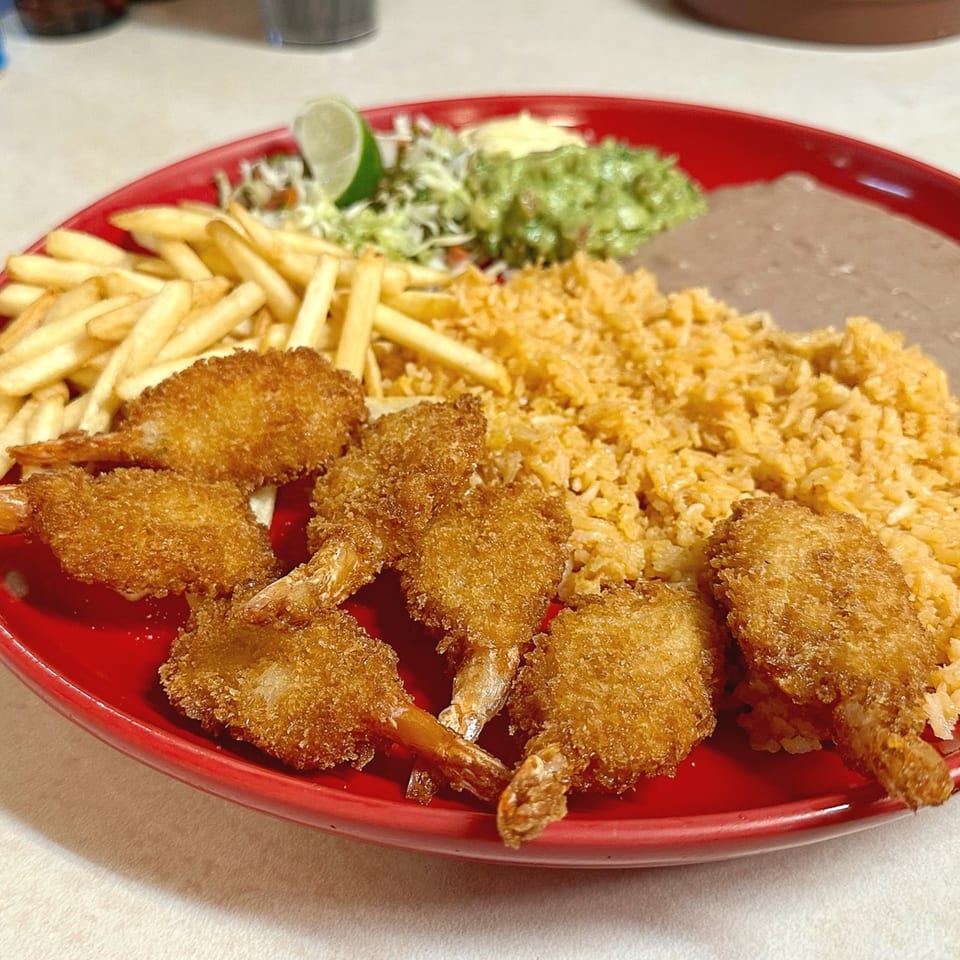 Tacos El Rey fried shrimp with rice, refried beans, french fries, guacamole, and lime on a red plate.
