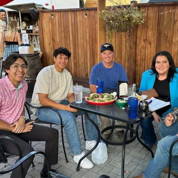 Four people smiling at a table with tacos and drinks on an outdoor patio at Tacos El Rey.