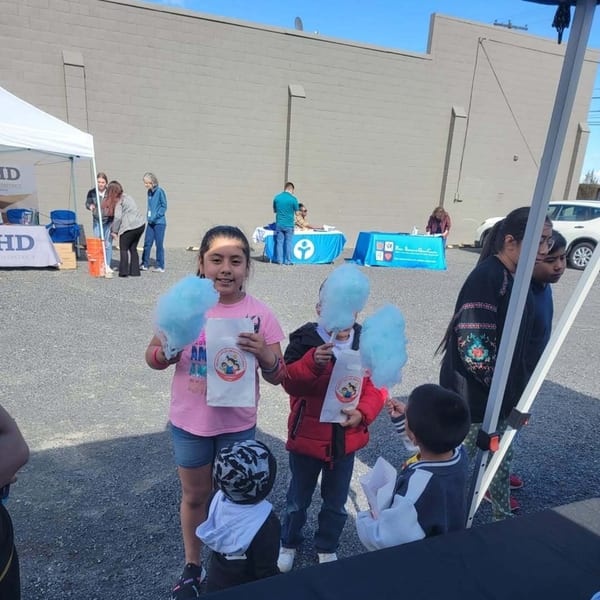 Children holding blue cotton candy and bags at an outdoor event with adults and tents.