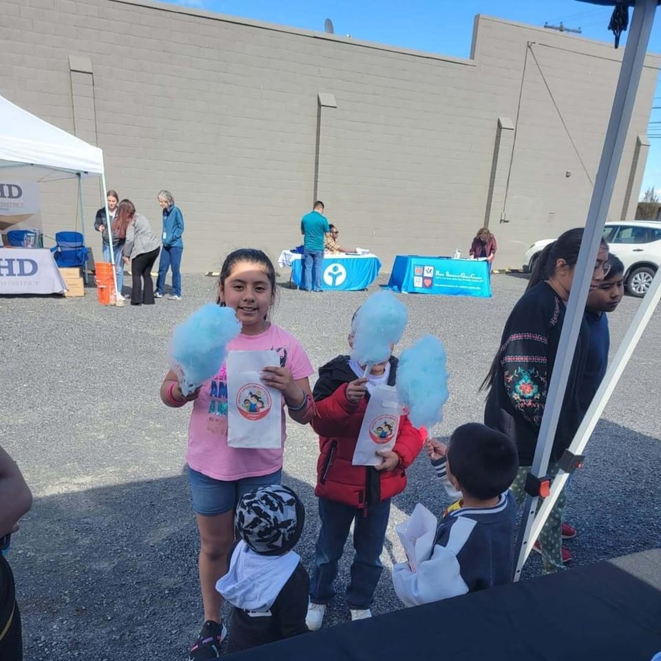 Children holding blue cotton candy and bags at an outdoor event with adults and tents.