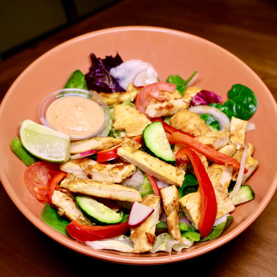 A vibrant chicken salad with bell peppers, cucumbers, and lime in an orange bowl.